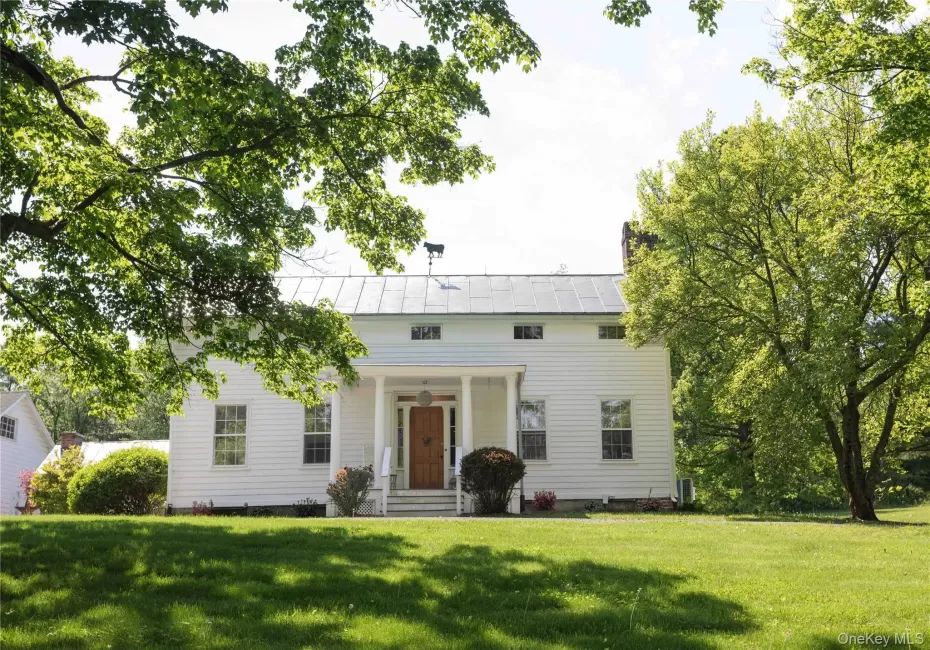 White siding exterior featuring a covered porch with white columns, a natural wood front door, and a metal roof White siding exterior featuring a covered porch with white columns, a natural wood front door, and a metal roof