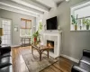 Spacious living area featuring exposed ceiling beams, wood-finish flooring, and a fireplace with a stone surround and white mantel Spacious living area featuring exposed ceiling beams, wood-finish flooring, and a fireplace with a stone surround and white mantel