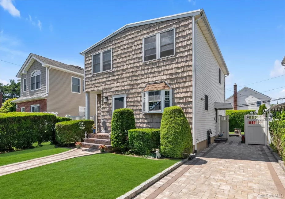Two-story residence featuring vinyl siding exterior, bay window, front entry with brick steps, paver driveway, and manicured lawn with mature hedges, Two-story residence featuring vinyl siding exterior, bay window, front entry with brick steps, paver driveway, and manicured lawn with mature hedges,