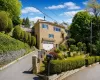 Brick façade residence featuring an integrated garage, a terraced front yard, established hedges, and a paved driveway with stone retaining walls Brick façade residence featuring an integrated garage, a terraced front yard, established hedges, and a paved driveway with stone retaining walls