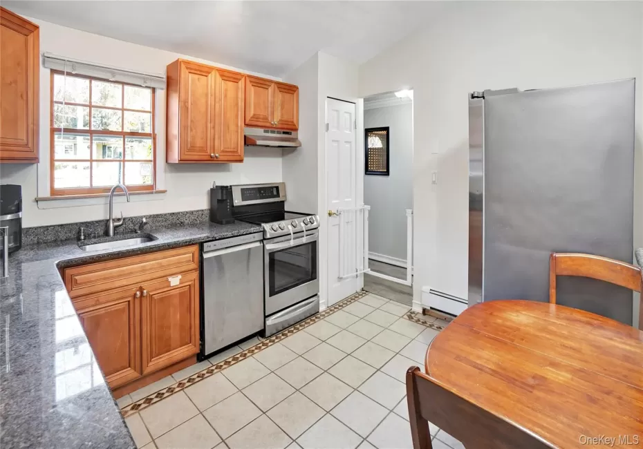 Kitchen with light tile patterned floors, brown cabinets, dark stone countertops, appliances with stainless steel finishes, and vaulted ceiling Kitchen with light tile patterned floors, brown cabinets, dark stone countertops, appliances with stainless steel finishes, and vaulted ceiling