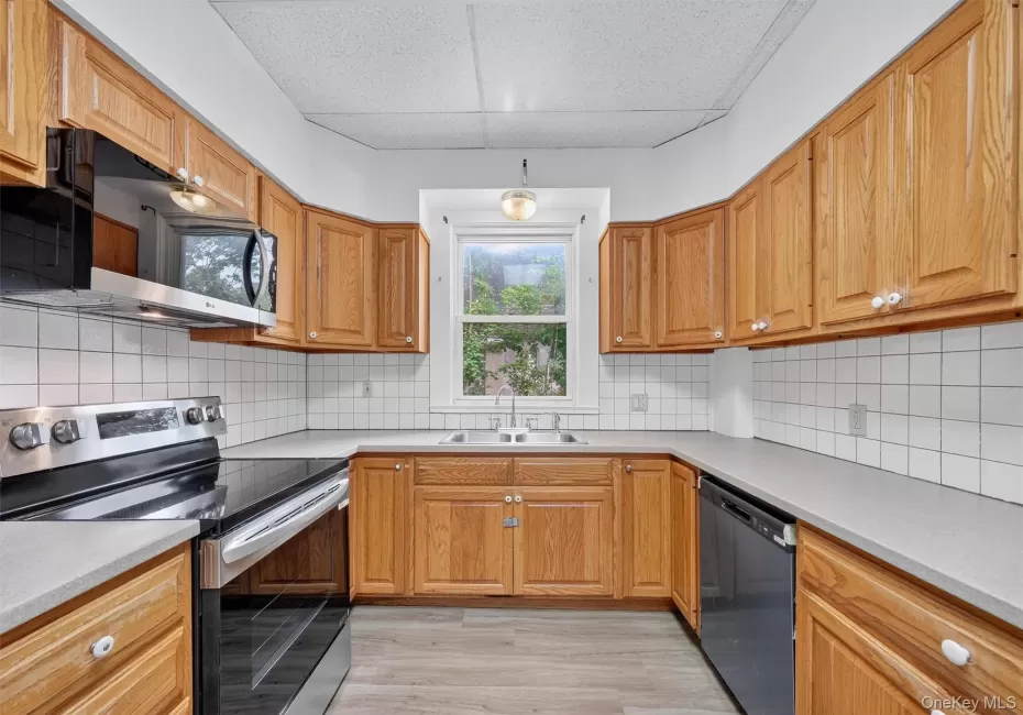 Kitchen featuring stainless steel range with electric cooktop, black microwave, dishwasher, light wood-style floors, and tasteful backsplash Kitchen featuring stainless steel range with electric cooktop, black microwave, dishwasher, light wood-style floors, and tasteful backsplash