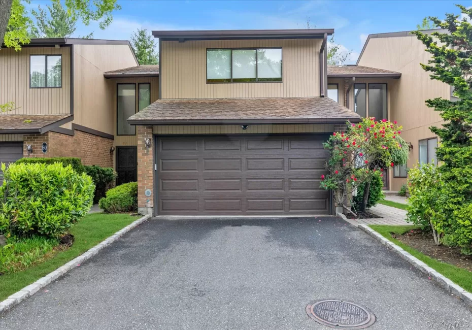 Two-story townhouse with a brown paneled garage door, asphalt driveway, and mature landscaping Two-story townhouse with a brown paneled garage door, asphalt driveway, and mature landscaping