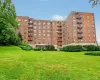 Brick multi-story building featuring multiple windows, exterior fire escapes, a recessed main entrance, and surrounding green landscaping Brick multi-story building featuring multiple windows, exterior fire escapes, a recessed main entrance, and surrounding green landscaping