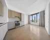 Open-concept living space with wood-finish flooring, a full kitchen, and a large window Open-concept living space with wood-finish flooring, a full kitchen, and a large window