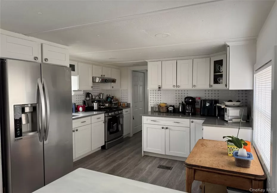 Kitchen with stainless steel appliances, dark vinyl floors, white cabinets, and backsplash Kitchen with stainless steel appliances, dark vinyl floors, white cabinets, and backsplash