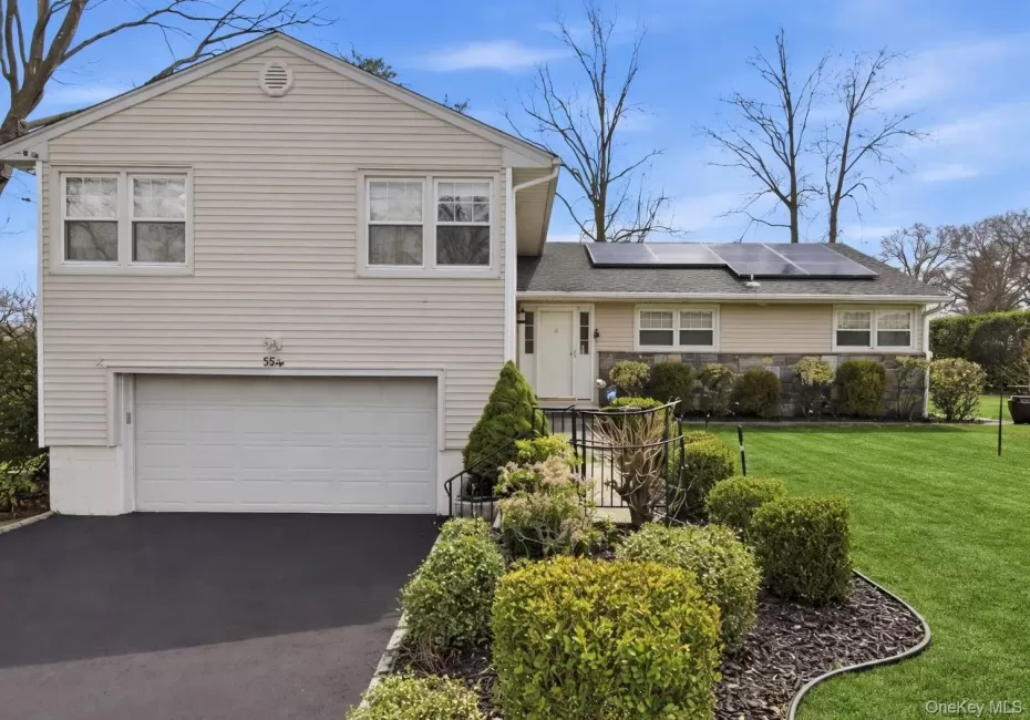 Split level home featuring an attached garage, driveway, a front yard, and roof mounted solar panels Split level home featuring an attached garage, driveway, a front yard, and roof mounted solar panels
