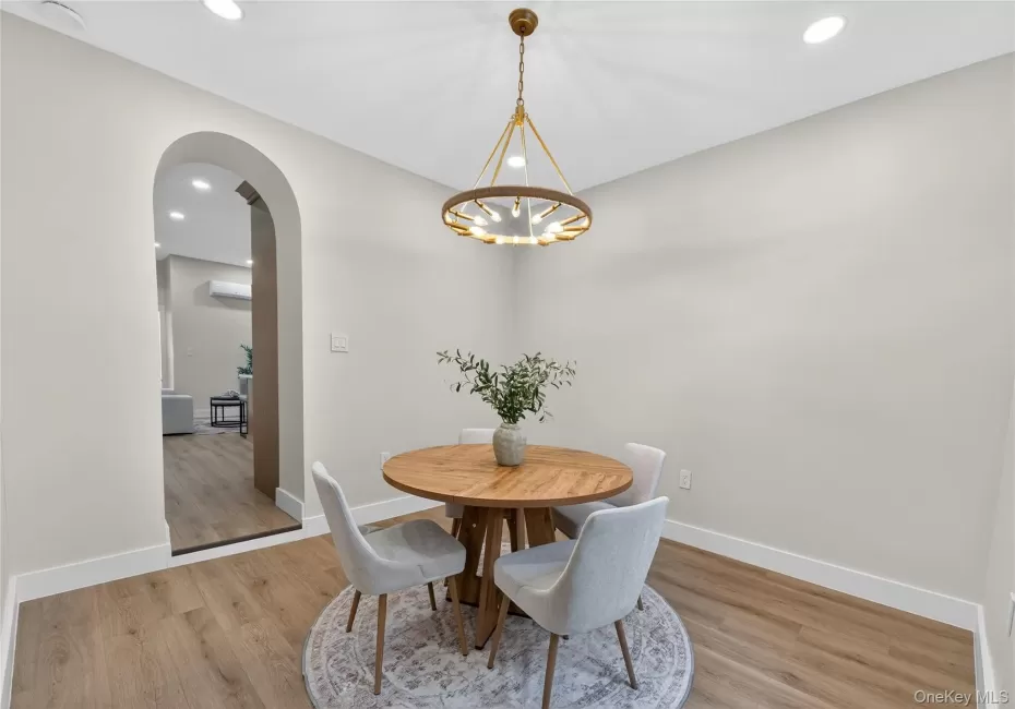 Dining area featuring a contemporary brass chandelier, wood-finish flooring, recessed ceiling lights, an arched entryway, and white baseboards Dining area featuring a contemporary brass chandelier, wood-finish flooring, recessed ceiling lights, an arched entryway, and white baseboards