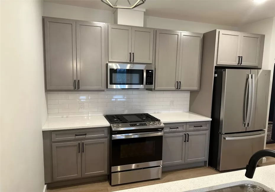 Kitchen featuring light gray shaker-style cabinetry, white subway tile backsplash, white quartz countertops, and stainless steel appliances. Kitchen featuring light gray shaker-style cabinetry, white subway tile backsplash, white quartz countertops, and stainless steel appliances.