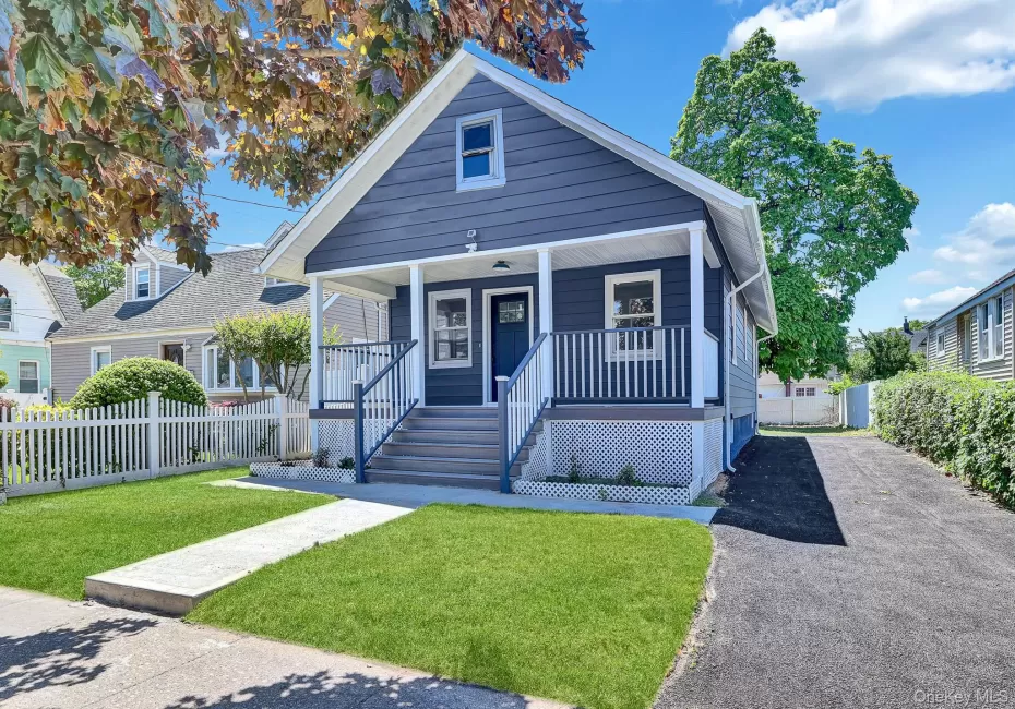 Charming blue-gray exterior with white trim, featuring a covered front porch with white railings and lattice detailing Charming blue-gray exterior with white trim, featuring a covered front porch with white railings and lattice detailing
