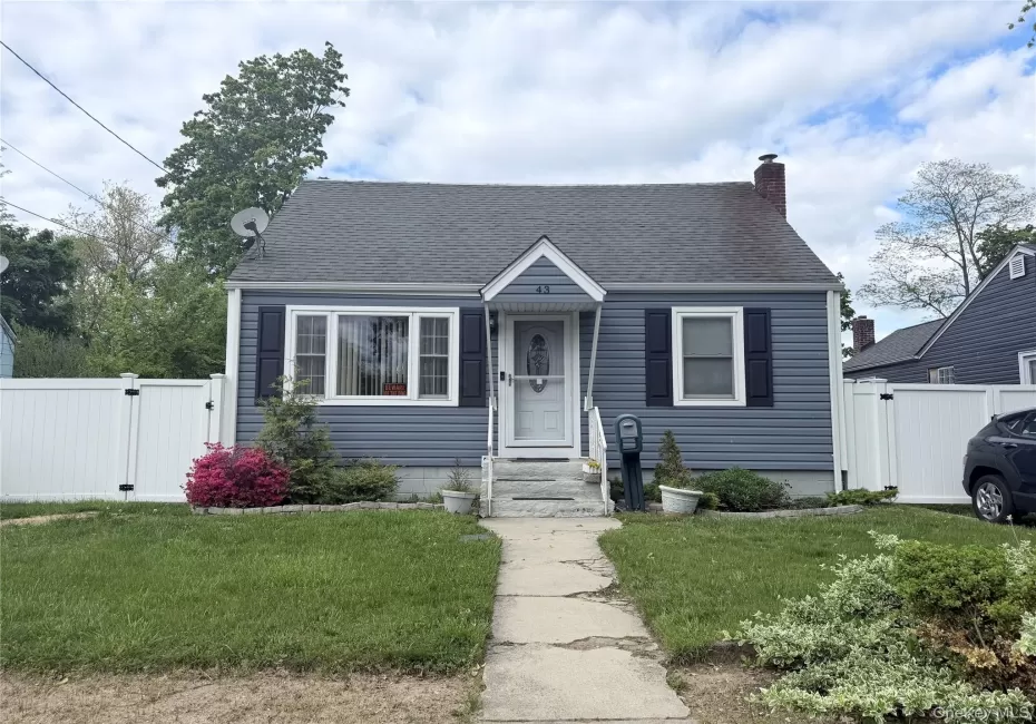 Charming residence featuring blue siding, a dark shingle roof, a brick chimney, and white privacy fencing Charming residence featuring blue siding, a dark shingle roof, a brick chimney, and white privacy fencing