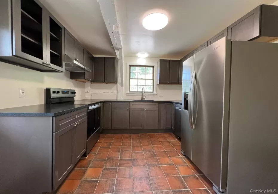 Kitchen featuring stainless steel appliances, dark countertops, under cabinet range hood, stone finish flooring, and open shelves Kitchen featuring stainless steel appliances, dark countertops, under cabinet range hood, stone finish flooring, and open shelves