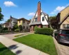 Tudor-style residence featuring a prominent brick chimney, multi-toned slate roof, and white siding with dark trim accents Tudor-style residence featuring a prominent brick chimney, multi-toned slate roof, and white siding with dark trim accents