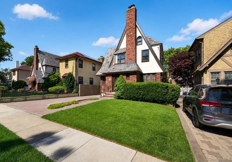 Tudor-style residence featuring a prominent brick chimney, multi-toned slate roof, and white siding with dark trim accents Tudor-style residence featuring a prominent brick chimney, multi-toned slate roof, and white siding with dark trim accents