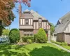 Tudor-style residence featuring brick and half-timbered facade, a prominent brick chimney, and a slate-style roof Tudor-style residence featuring brick and half-timbered facade, a prominent brick chimney, and a slate-style roof