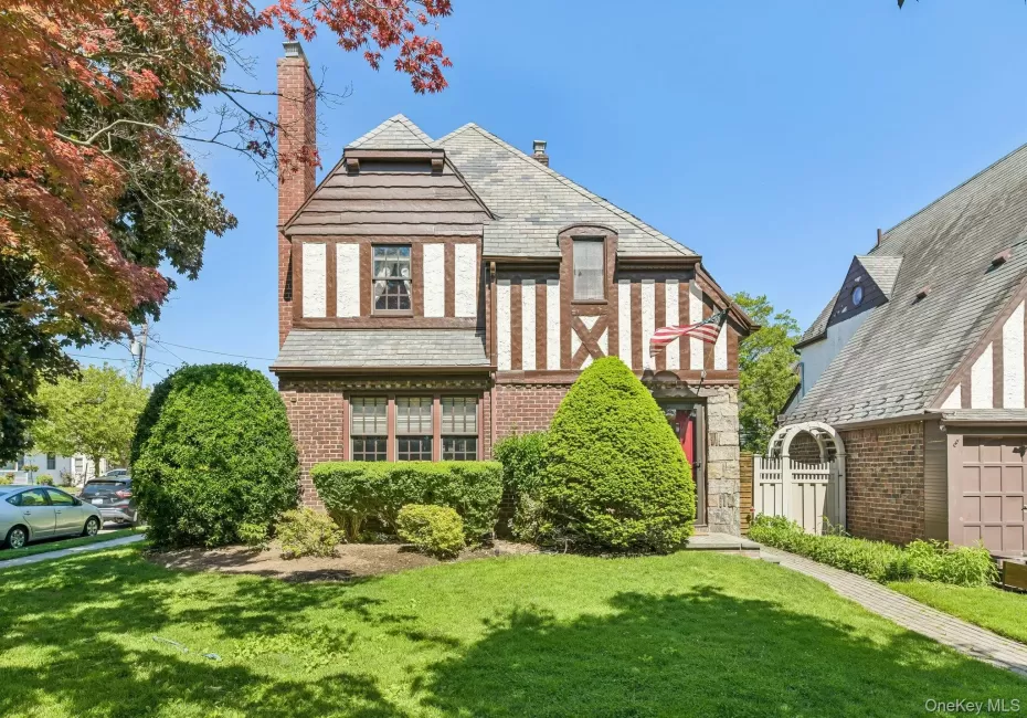 Tudor-style residence featuring brick and half-timbered facade, a prominent brick chimney, and a slate-style roof Tudor-style residence featuring brick and half-timbered facade, a prominent brick chimney, and a slate-style roof