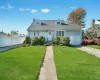 Light blue siding residence featuring a front lawn with a concrete walkway, a white privacy fence, a driveway, and an attached garage Light blue siding residence featuring a front lawn with a concrete walkway, a white privacy fence, a driveway, and an attached garage