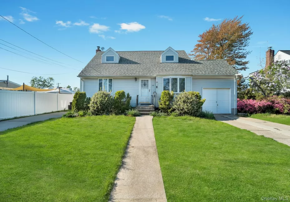 Light blue siding residence featuring a front lawn with a concrete walkway, a white privacy fence, a driveway, and an attached garage Light blue siding residence featuring a front lawn with a concrete walkway, a white privacy fence, a driveway, and an attached garage