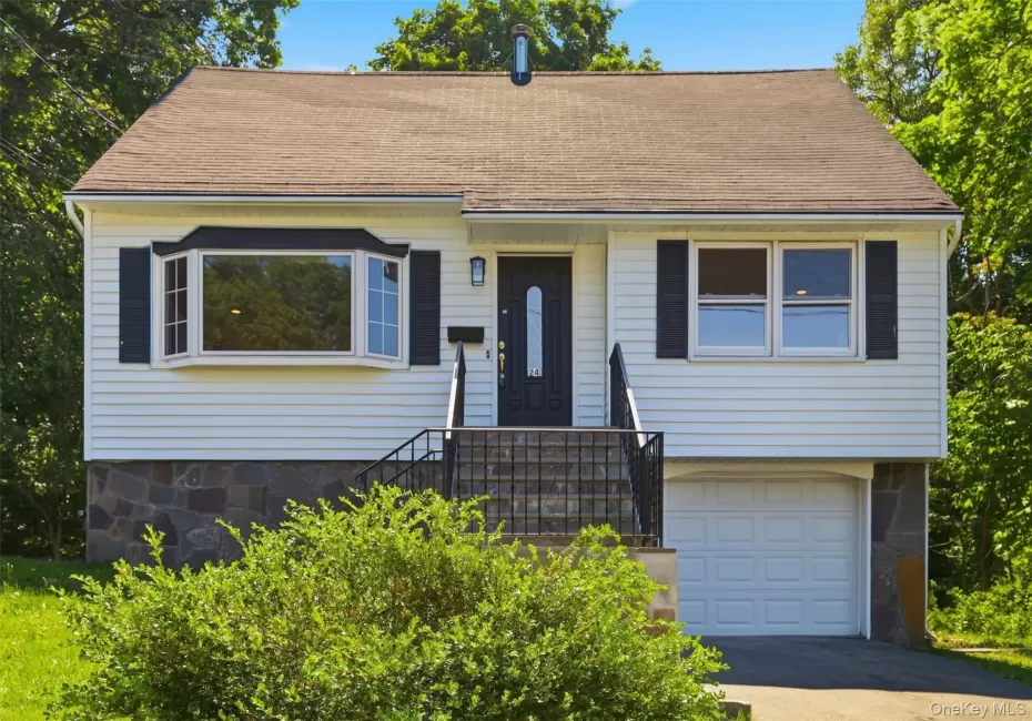 White siding exterior with a stone veneer foundation, featuring a prominent bay window with black shutters, a dark entry door with a decorative glass insert, and an integrated garage with a white panel door White siding exterior with a stone veneer foundation, featuring a prominent bay window with black shutters, a dark entry door with a decorative glass insert, and an integrated garage with a white panel door