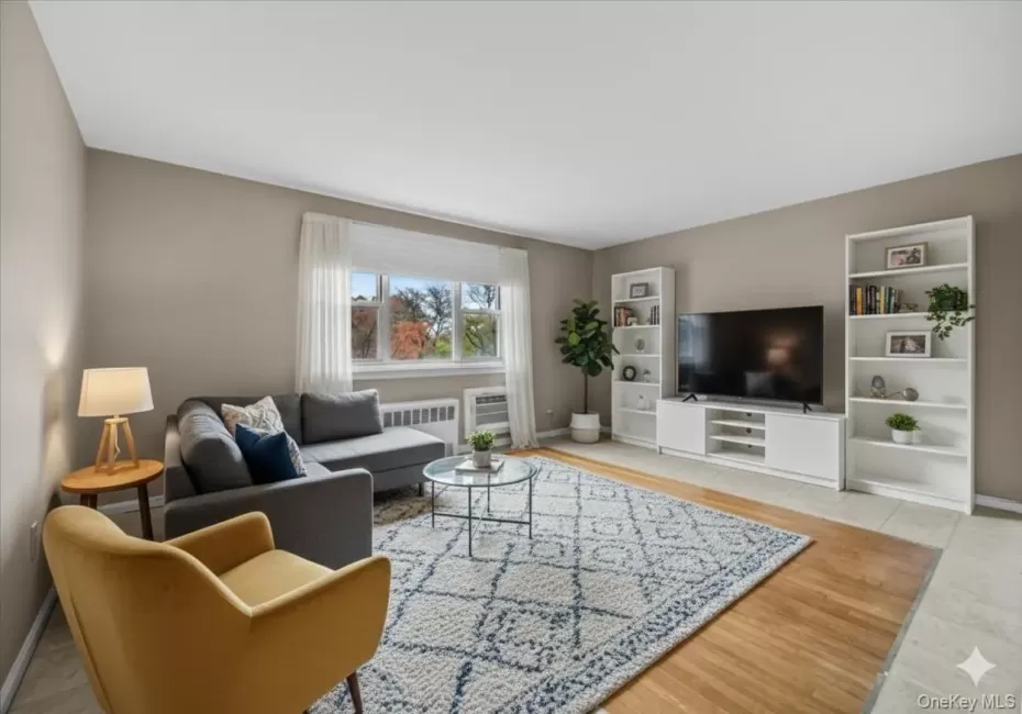 Living room featuring radiator, light tile patterned flooring, and a wall unit AC Living room featuring radiator, light tile patterned flooring, and a wall unit AC