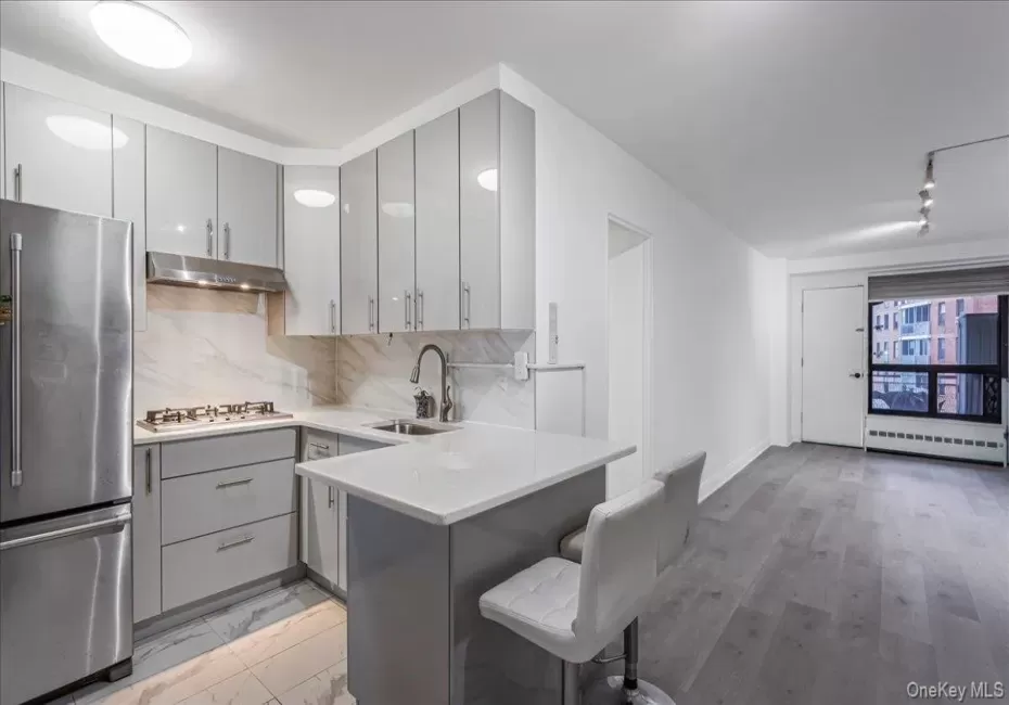 Kitchen with gray cabinetry, stainless steel appliances, tasteful backsplash, and a breakfast bar Kitchen with gray cabinetry, stainless steel appliances, tasteful backsplash, and a breakfast bar