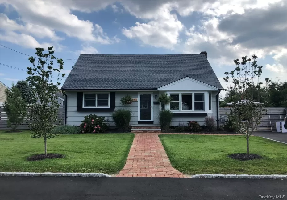 Charming residence featuring a light gray exterior, dark gray shingle roof, and a red brick paver walkway leading to the front entry Charming residence featuring a light gray exterior, dark gray shingle roof, and a red brick paver walkway leading to the front entry