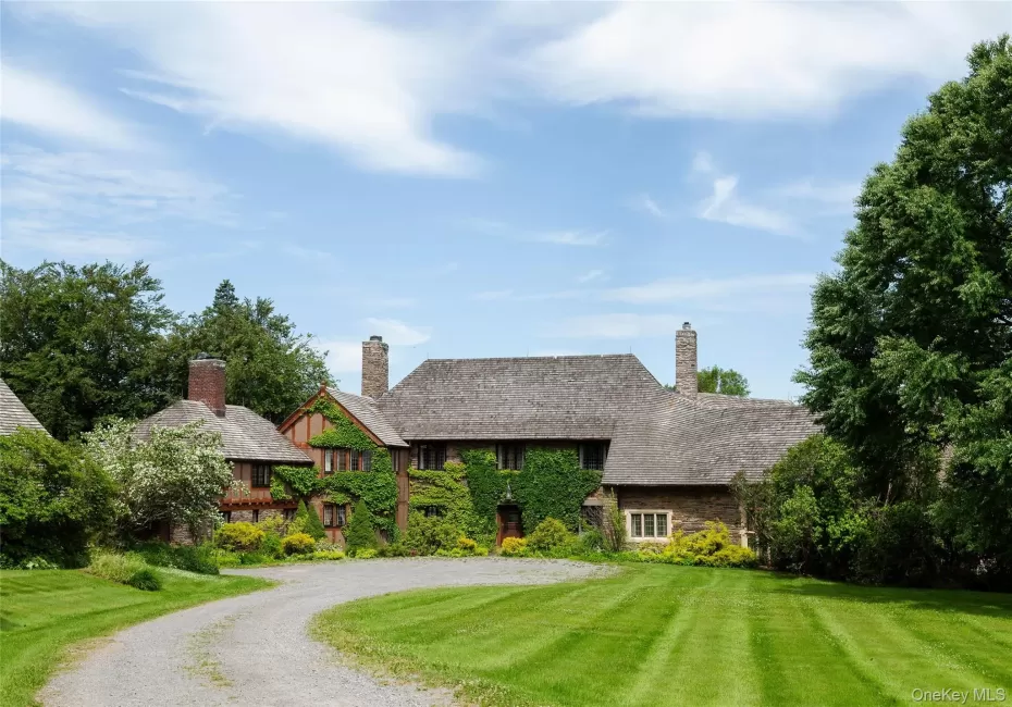 Tudor-style house with a chimney, a front lawn, driveway, and stone siding Tudor-style house with a chimney, a front lawn, driveway, and stone siding