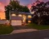 Split-level residence featuring gray siding, a two-car garage with white doors, and a paved driveway Split-level residence featuring gray siding, a two-car garage with white doors, and a paved driveway