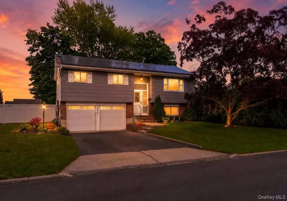 Split-level residence featuring gray siding, a two-car garage with white doors, and a paved driveway Split-level residence featuring gray siding, a two-car garage with white doors, and a paved driveway