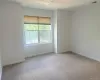 Room featuring neutral carpeting, white painted walls, a large multi-pane window, and a ceiling-mounted light fixture Room featuring neutral carpeting, white painted walls, a large multi-pane window, and a ceiling-mounted light fixture
