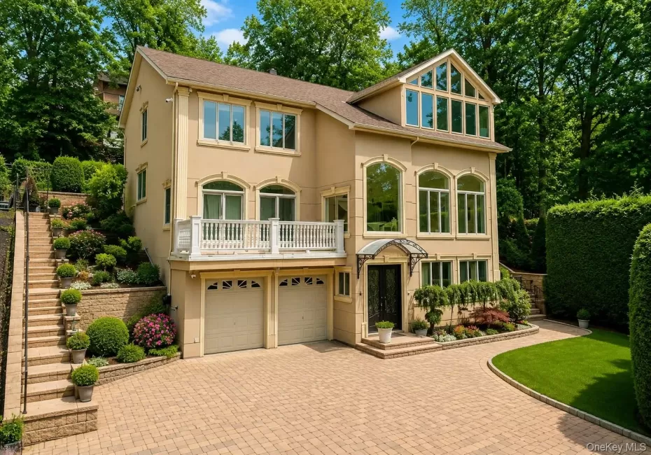 Stucco exterior with multiple arched windows, prominent balcony with white railing, and an expansive paved driveway Stucco exterior with multiple arched windows, prominent balcony with white railing, and an expansive paved driveway