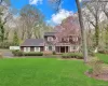 Colonial-style exterior featuring a wood shingle facade, a covered front porch with white columns, and a mature flowering tree Colonial-style exterior featuring a wood shingle facade, a covered front porch with white columns, and a mature flowering tree