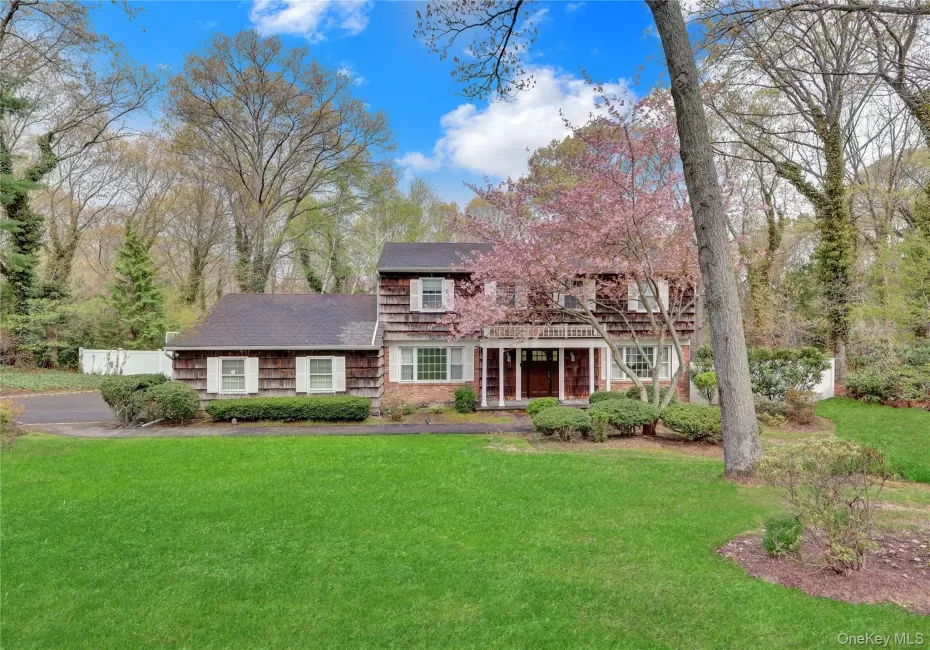 Colonial-style exterior featuring a wood shingle facade, a covered front porch with white columns, and a mature flowering tree Colonial-style exterior featuring a wood shingle facade, a covered front porch with white columns, and a mature flowering tree