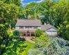 Traditional colonial two-story residence featuring light-colored siding, a covered entry porch, a multi-car garage, mature landscaping, and a paver walkway Traditional colonial two-story residence featuring light-colored siding, a covered entry porch, a multi-car garage, mature landscaping, and a paver walkway