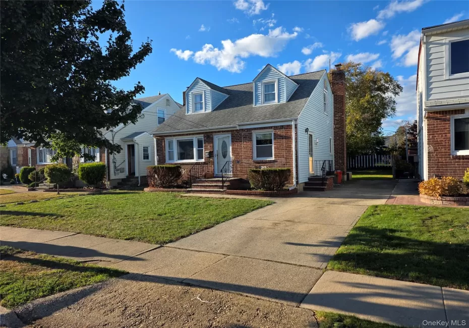 Cape cod house featuring roof with shingles, a front lawn, brick siding, a chimney, and concrete driveway Cape cod house featuring roof with shingles, a front lawn, brick siding, a chimney, and concrete driveway