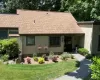 Exterior featuring a composite shingle roof, vertical siding, a paved walkway, established landscaping, and a covered entryway Exterior featuring a composite shingle roof, vertical siding, a paved walkway, established landscaping, and a covered entryway