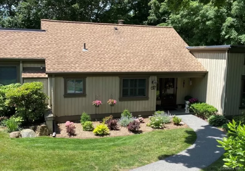 Exterior featuring a composite shingle roof, vertical siding, a paved walkway, established landscaping, and a covered entryway Exterior featuring a composite shingle roof, vertical siding, a paved walkway, established landscaping, and a covered entryway