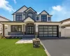 Magnificent contemporary two-story home featuring a stone and siding exterior, multi-pane black garage door, paved driveway, manicured lawn, and a covered entry with wood-finish columns Magnificent contemporary two-story home featuring a stone and siding exterior, multi-pane black garage door, paved driveway, manicured lawn, and a covered entry with wood-finish columns