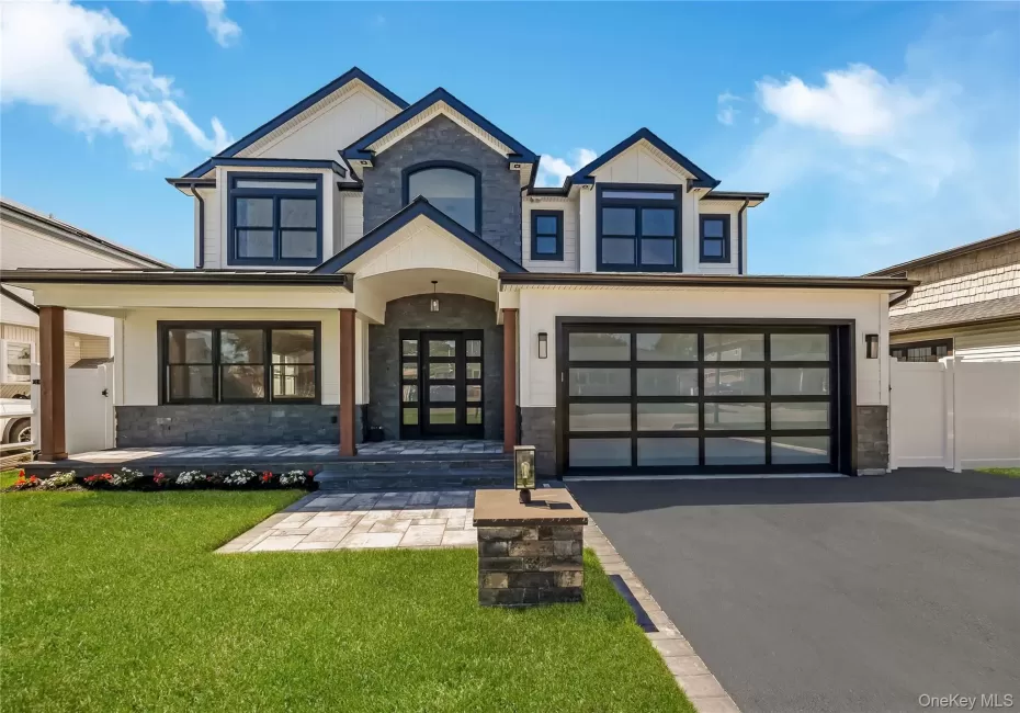 Magnificent contemporary two-story home featuring a stone and siding exterior, multi-pane black garage door, paved driveway, manicured lawn, and a covered entry with wood-finish columns Magnificent contemporary two-story home featuring a stone and siding exterior, multi-pane black garage door, paved driveway, manicured lawn, and a covered entry with wood-finish columns