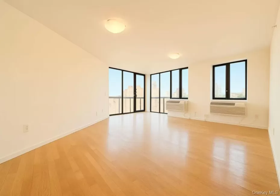 Unfurnished room with light wood-style flooring, a wall of windows, and a wall mounted air conditioner Unfurnished room with light wood-style flooring, a wall of windows, and a wall mounted air conditioner