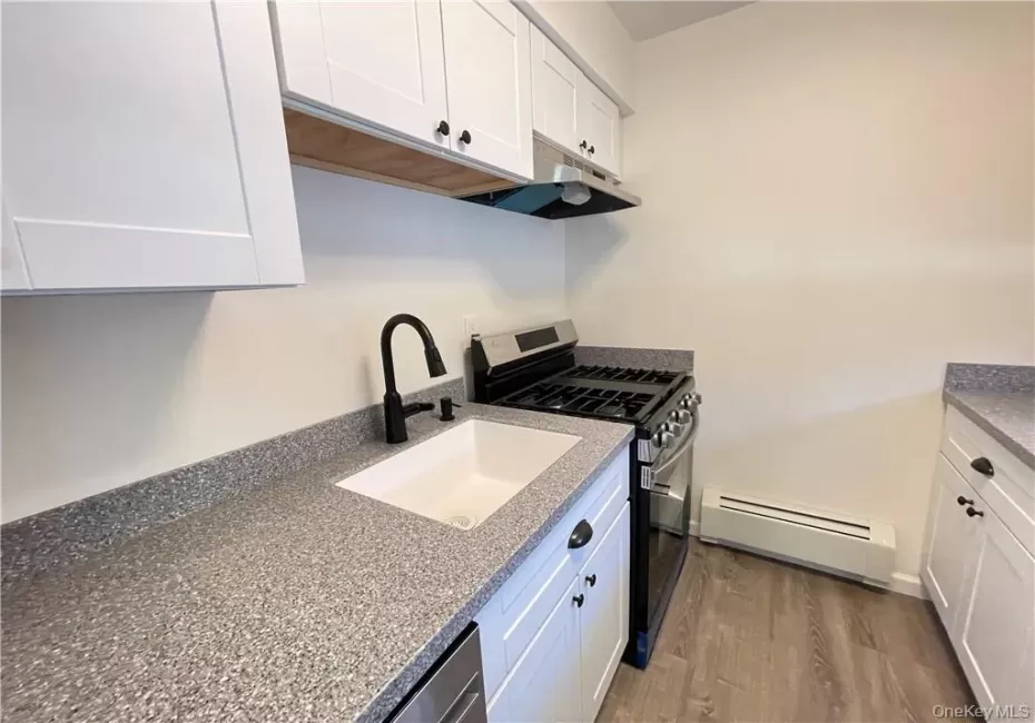 Kitchen featuring white shaker-style cabinetry, speckled countertops, a matte black gooseneck faucet, a stainless steel range, and wood-finish flooring Kitchen featuring white shaker-style cabinetry, speckled countertops, a matte black gooseneck faucet, a stainless steel range, and wood-finish flooring