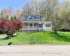 Two-story residence featuring light-colored siding, a covered front porch with white railings, and dark louvered shutters Two-story residence featuring light-colored siding, a covered front porch with white railings, and dark louvered shutters