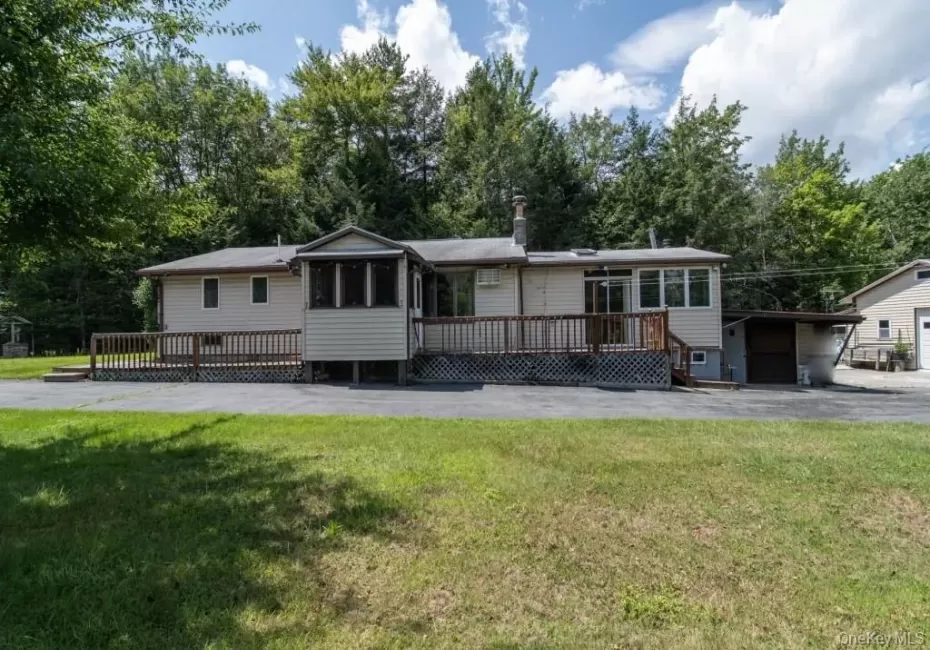 Back of house featuring a deck, a yard, view of scattered trees, and driveway Back of house featuring a deck, a yard, view of scattered trees, and driveway