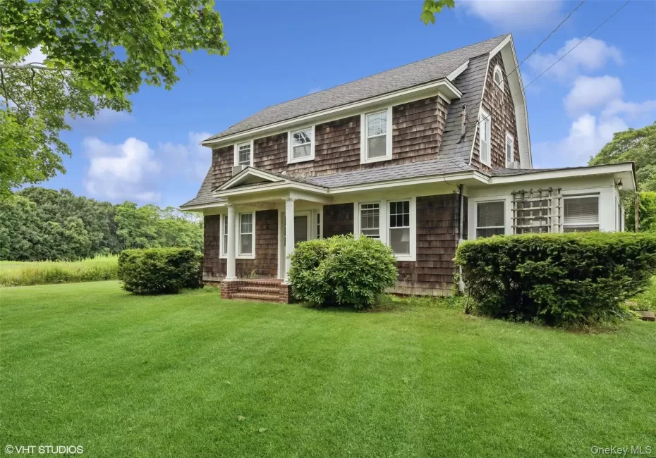 Shingle-style home with a front yard, a shingled roof, and a gambrel roof Shingle-style home with a front yard, a shingled roof, and a gambrel roof