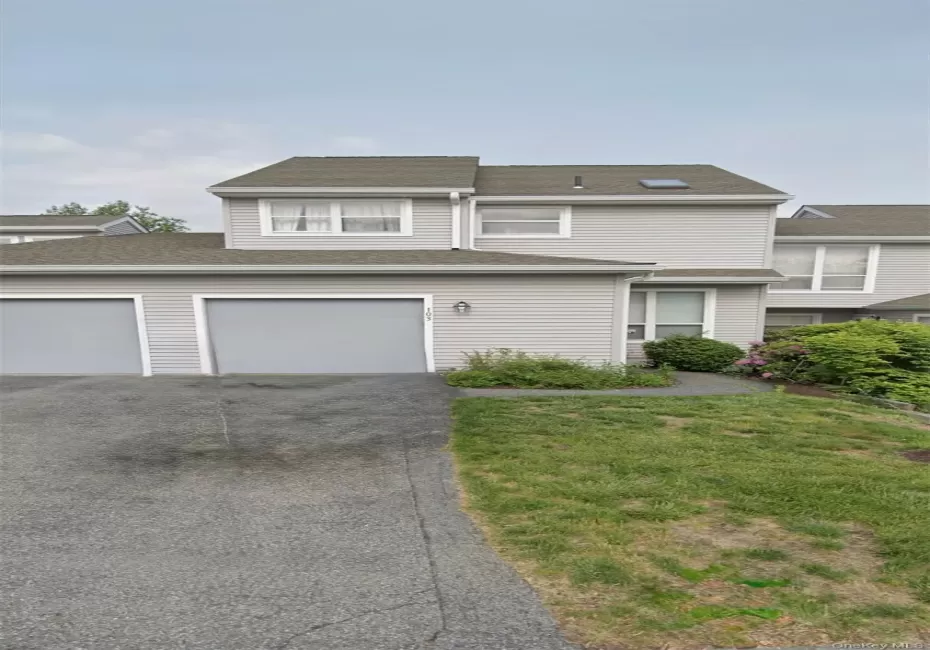 Light gray-sided townhouse with dual garage doors and an asphalt driveway Light gray-sided townhouse with dual garage doors and an asphalt driveway