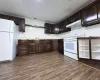 Kitchen featuring wood-finish flooring, dark wood cabinetry, and white appliances Kitchen featuring wood-finish flooring, dark wood cabinetry, and white appliances