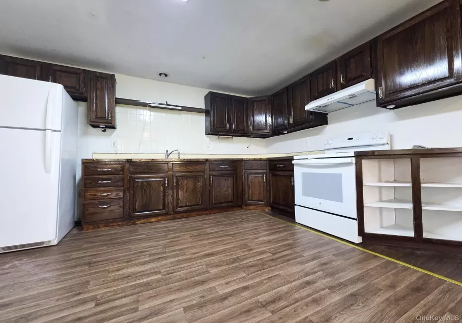 Kitchen featuring wood-finish flooring, dark wood cabinetry, and white appliances Kitchen featuring wood-finish flooring, dark wood cabinetry, and white appliances