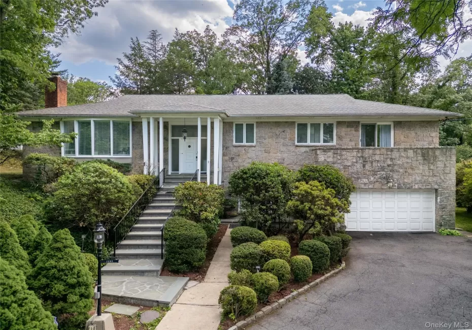 Stone facade residence featuring a prominent front entrance with white columns, a two-car garage, and extensive mature landscaping. Stone facade residence featuring a prominent front entrance with white columns, a two-car garage, and extensive mature landscaping.