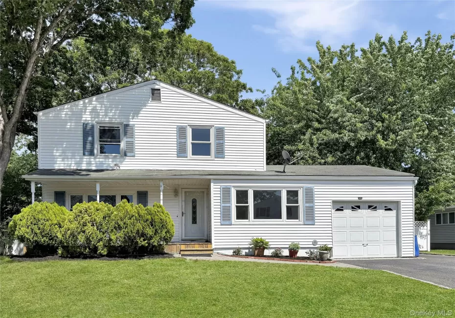 White siding exterior with blue window shutters, featuring a covered front porch, an attached garage, a paved driveway White siding exterior with blue window shutters, featuring a covered front porch, an attached garage, a paved driveway
