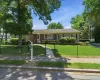 Ranch-style residence featuring a well-maintained lawn, mature trees, and a black chain-link fence Ranch-style residence featuring a well-maintained lawn, mature trees, and a black chain-link fence